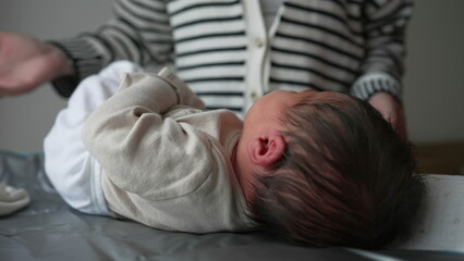 Mother gently dresses a newborn baby on a changing mat, adjusting the clothing with care. infant...