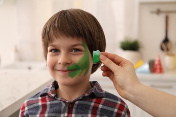 Animator drawing dinosaur on boy's face indoors, closeup