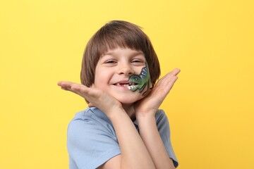 Cute boy with dinosaur face painting on yellow background