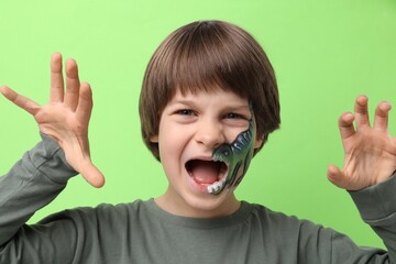 Cute boy with dinosaur face painting posing on light green background