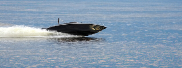 Black motorboat. The boat is sailing at high speed. Panoramic photo.