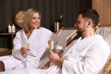Happy couple in bathrobes with glasses of champagne relaxing in spa salon