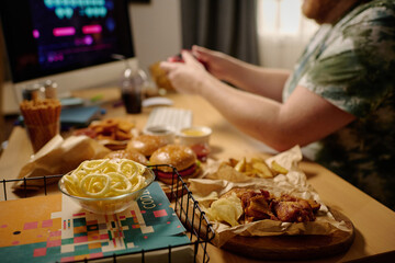 Individual engrossed in gaming on computer surrounded by various snacks including fries and...