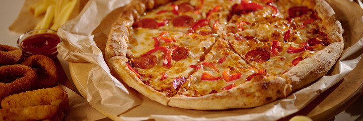 Delicious pepperoni pizza with melted cheese and red peppers, served with a side of crispy onion rings and French fries, creating an appetizing meal setting