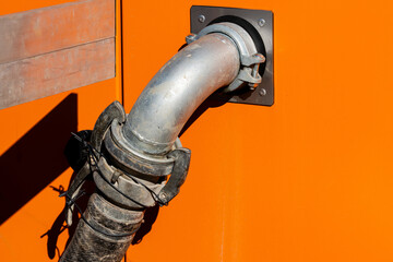 Metal pipe connected to an orange tank for fluid transfer. Close-up.