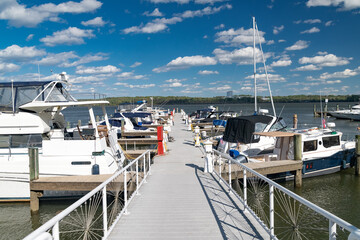 Fototapeta premium Wooden pier walkway leading to boats and yachts moored at the marina in Annapolis, Maryland. Blue sky with clouds.