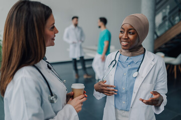 Two female doctors talking during coffee break in hospital hallway