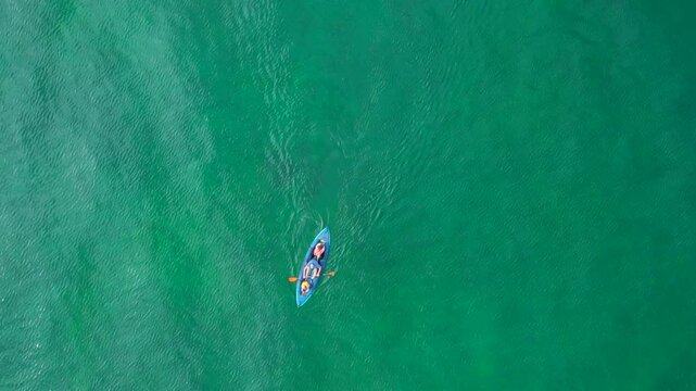 Aerial drone view of a canoe with a family having fun sailing the crystal clear waters of the sea