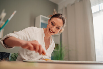 Smiling artist painting on canvas at home studio enjoying creative hobby