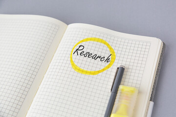 Open squared notebook with handwritten word research circled in yellow marker, pen, highlighter and...