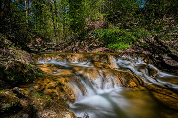 Cascading water flows over rocks in a peaceful forest setting, creating a tranquil natural scene