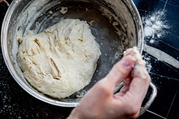 Homemade Pizza Preparation with Three Cheeses – Female Hands in Action. A warm, close-up scene of a woman’s hands preparing homemade pizza dough on a kitchen countertop. Photo recipe.