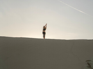 A woman stands joyfully on top of a sand dune, embracing the serene atmosphere in desert during...