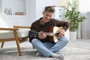 Happy man playing guitar on floor indoors