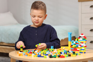 Fototapeta premium Cute boy playing with building blocks at wooden table indoors