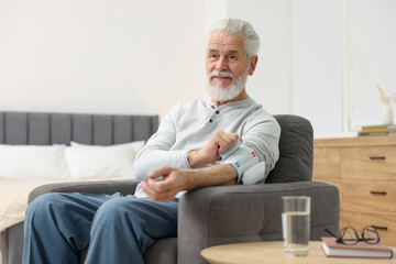 Senior man measuring blood pressure in armchair at home