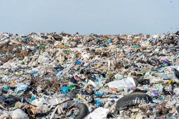 Large piles of mixed waste and debris visible at a landfill site under clear skies show the impact of pollution and waste management issues