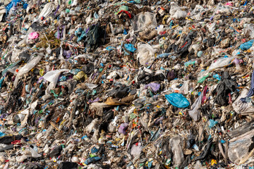 Large mound of mixed waste materials including plastic, cloth, and organic matter creates serious...
