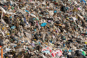 A massive landfill site showcases a mountain of garbage filled with plastic waste, old materials, and various discarded items under bright sunlight