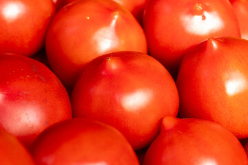 Ripe tomatoes in close proximity, displaying a shiny surface and rich red hue in a market setting during daylight