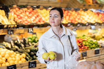 Portrait of female shopper carefully selecting ripe apples on a supermarket display