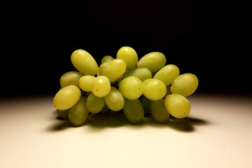Close-up of fresh green grapes cluster on a neutral surface with dark background. Minimalist still life of organic fruit with natural texture and soft shadows, illuminated by warm directional light