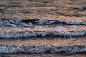 Close-up of gentle waves rolling across the surface of the sea at dusk. The soft lighting reflects off the water, creating peaceful and serene atmosphere