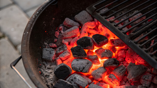Top-down view of glowing charcoal briquettes in a barbecue. with bright red embers and blackened surface.