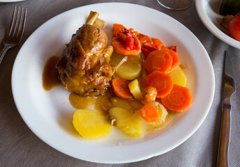 Juicy baked pork knuckle on bone served with baked potatoes and carrot on plate