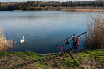 Fishing rods and equipment stand on a stand near the water on the river bank on a sunny day.