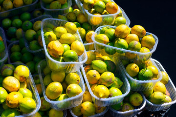 Vibrant assortment of lemons and limes packed closely in plastic containers, highlighting their...