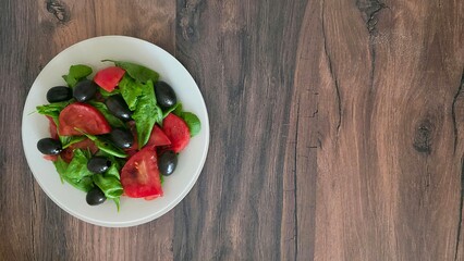 Fresh salad with spinach, tomatoes, olives, and soy sauce on a rustic wooden table. Healthy, light meal. Top view, copy space. Delicious vegetarian appetizer.
