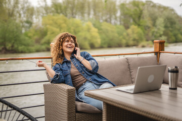 happy woman sit on the terrace talk on mobile phone and work on laptop