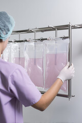 A person wearing gloves and a cap is handling pink liquid-filled bags on a metal rack. Laboratory setup and precision work