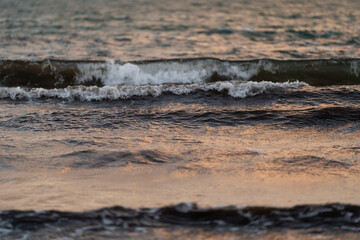 Close-up of gentle waves rolling across the surface of the sea at dusk. The soft lighting reflects off the water, creating peaceful and serene atmosphere