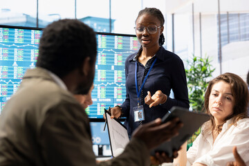 Business professional staff gather to review project development progress, analyzing detailed reports and statistics on interactive board to ensure strategic objectives. Diverse work team in meeting.