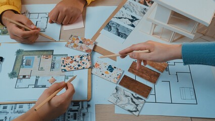 Hands actively participate in a dynamic interior design session, exploring vibrant materials and detailed floor plans, emphasizing teamwork and creativity in design. SACTR