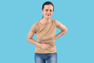 Young beautiful woman suffering from abdominal pain on blue background