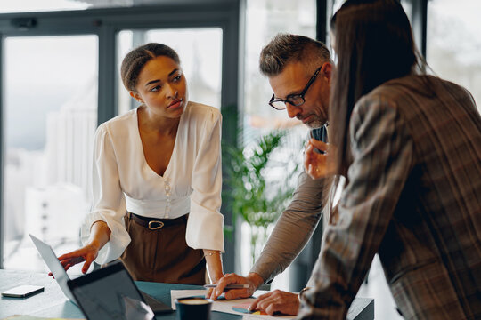 Professionals engage in discussion while collaborating over a laptop in a contemporary office environment.