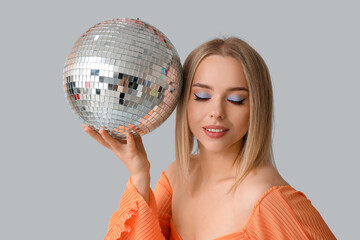 Beautiful young woman with disco ball on grey background