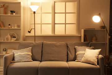 Interior of dark living room with sofa and glowing lamps in evening