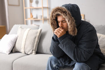 Frozen young man in puffer jacket at home