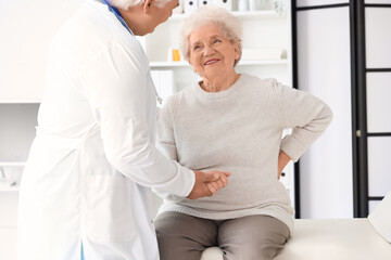 Obraz premium Sick senior woman with back pain visiting doctor in clinic