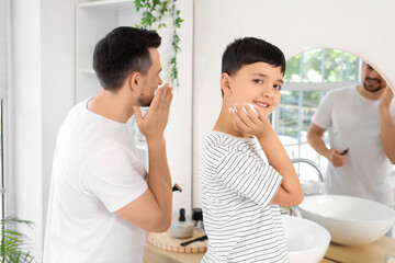 Happy father and his little son applying shaving foam on faces in bathroom