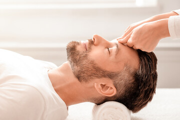 Side view of bearded middle aged man having relaxing head massage at white modern spa....