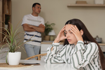 Upset young woman after quarrel with her husband sitting at table in kitchen