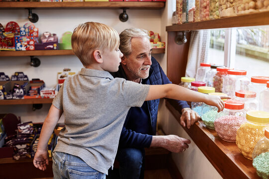 Man, child and jar candy store with point for gift, shopping and choice with love, care and bonding. Grandfather, boy kid and retail shop with container for sweets, decision and present with family