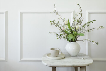 Spring, mothers day breakfast still life. Cup of coffee tea, marble table. Pink tulips, white blooming cherry plum tree branches in vase Elegant white classic stucco decor wall background. Living room