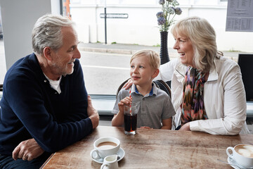 Senior man, woman and child in coffee shop, drink and soda with funny talk, vacation and relax with care. Grandparents, family and boy with glass, tea cup and matcha with smile, laugh or conversation