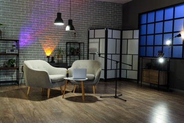 Interior of dark studio with podcaster's workplace, shelf units and glowing lamps